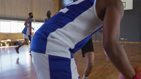 Diverso-Equipo-Masculino-De-Baloncesto-Y-Entrenador-Jugando-Partidos,-Usando-Máscaras-Faciales