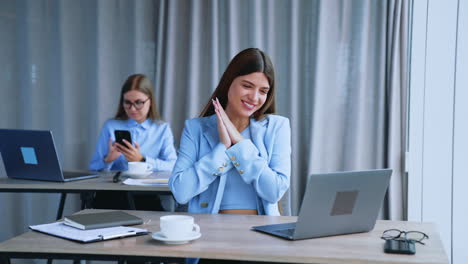 beautiful brunette girl working in the office is clapping her hands happily excited by something. lady at backdrop looks at her phone. blurred background.