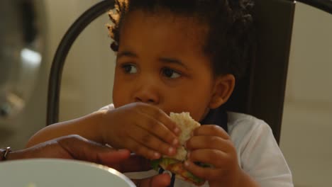 primer plano de un pequeño hijo negro lindo comiendo comida en la mesa de comedor en la cocina de una casa cómoda 4k