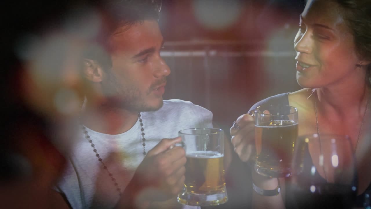 Man lifting beer mug and woman stirring initiating intimate chat in bar, bokeh highlighting mugs