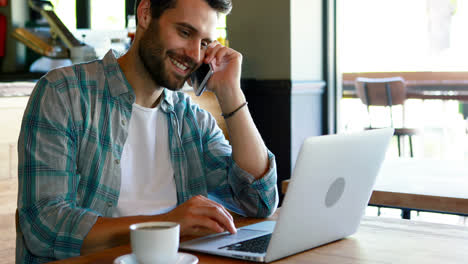 hombre hablando en teléfono móvil mientras usa una computadora portátil