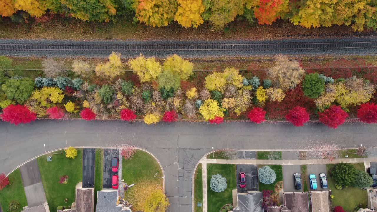 una impresionante toma aérea de arriba hacia abajo de un barrio canadiense junto a una vía férrea, con árboles de colores otoñales que separan la carretera y las vías