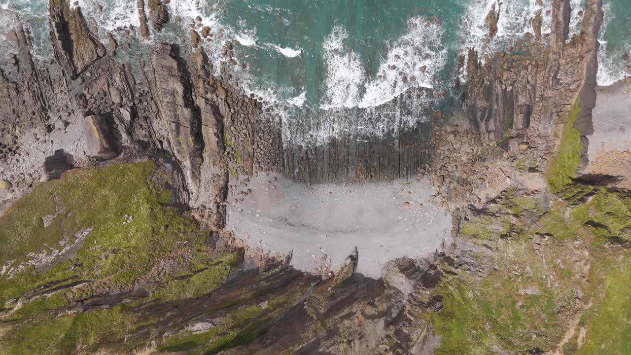Top-down aerial push-in of waves crashing against the North Atlantic coastline of England, showcasing the rugged shore and dynamic ocean