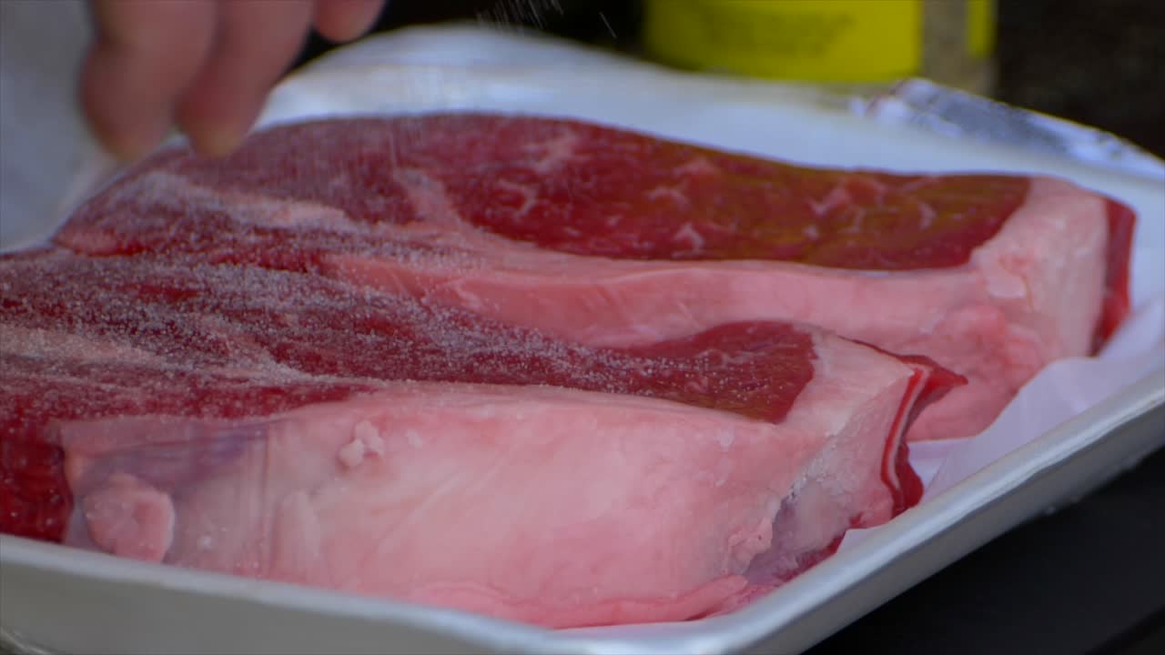 una mano vierte sal sobre un filete de costilla crudo