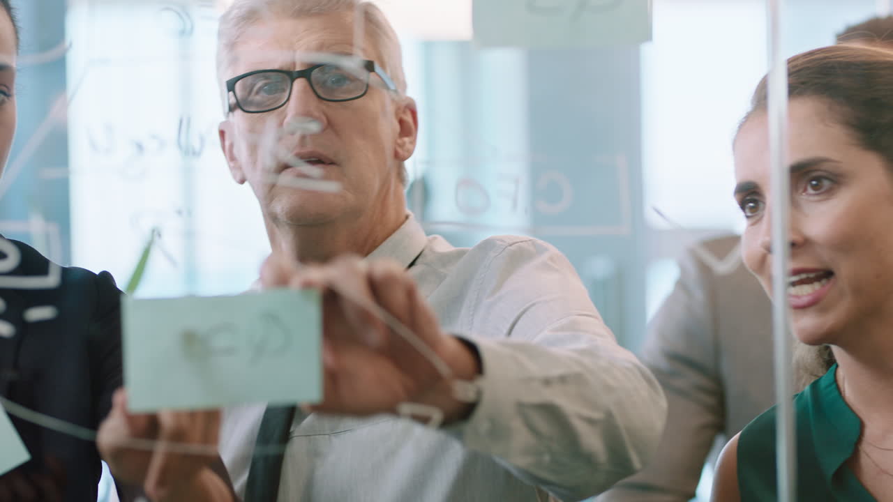 business team meeting using sticky notes brainstorming colleagues working on problem solving strategy writing on glass whiteboard thinking of solution for project in office through glass