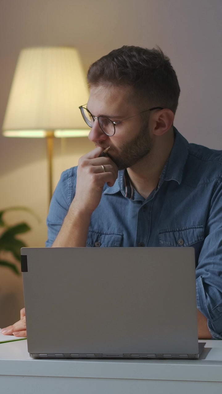 Giovane uomo con occhiali che lavora al computer portatile da casa