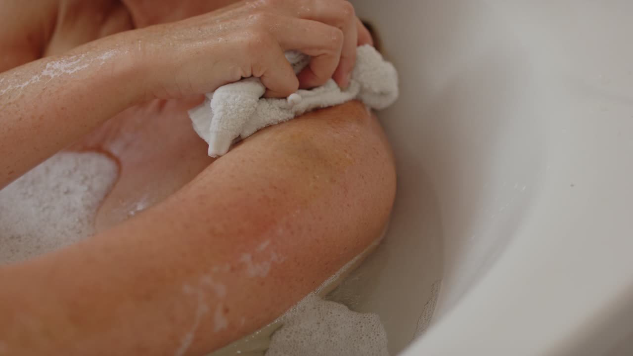 Attractive woman relaxing in bath scrubbing her arm with washcloth