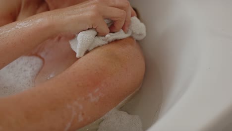 attractive woman relaxing in bath scrubbing her arm with washcloth