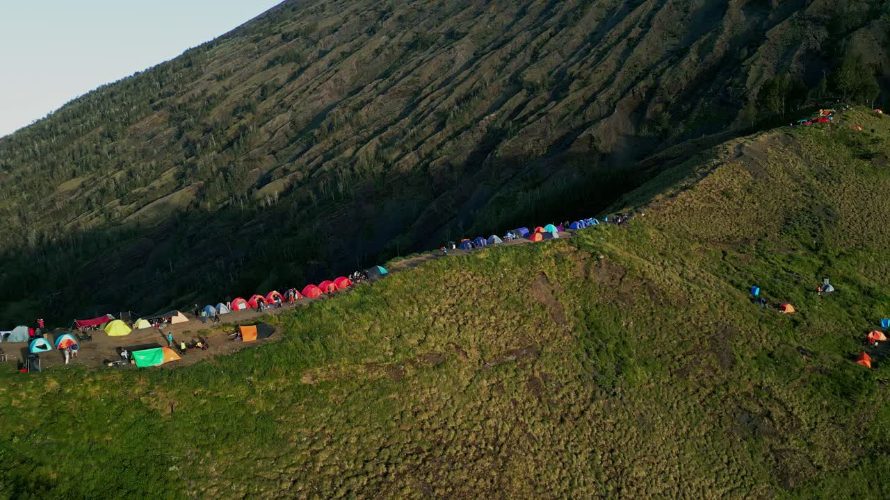 Campsite set on Mount Rinjani with several colorful tents surrounded by misty mountain air and peaceful natural scenery as trekkers prepare for summit hike.