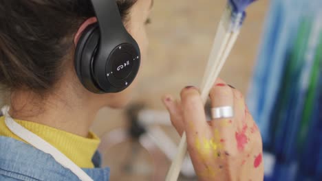 video de una artista biracial con auriculares pintando en el estudio