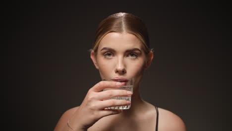 serious woman takes a sip out of a transparent water glass, black background