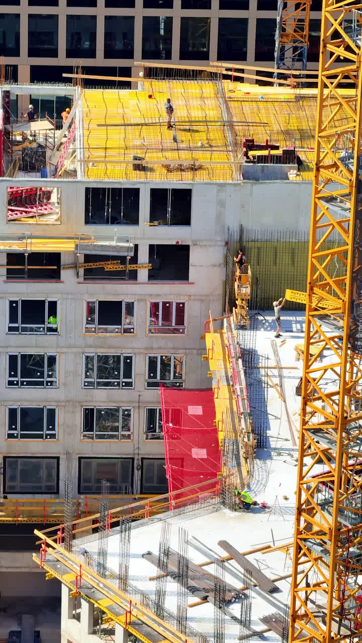 Daytime urban construction site. Workers are actively constructing a multi-story building in a busy city, surrounded by cranes and scaffolding