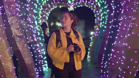 traveling asian woman with camera looking amazed at colorful illuminations at night