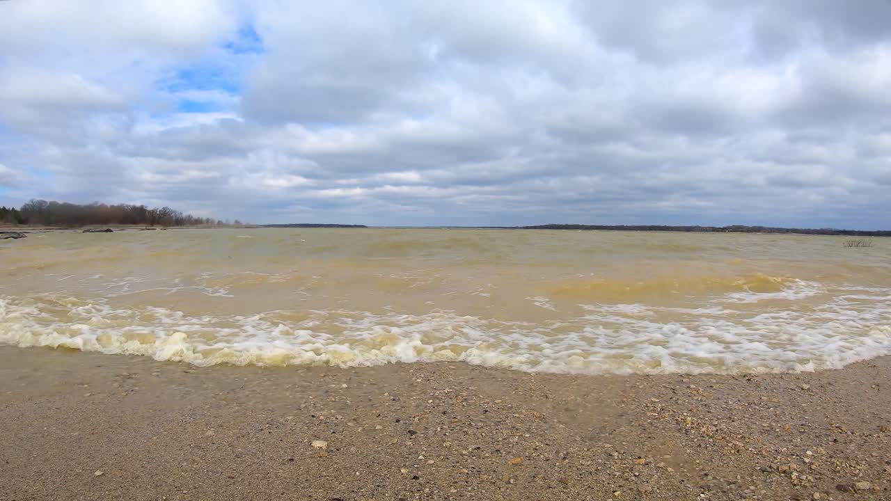 Strong winds after winter storm causes muddy ocean like waves to crash on a small beach on a Texas lake near a public marina