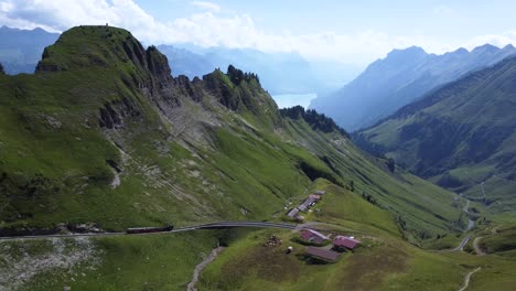 a train on track in the middle of the alps of switzerland, driving down from brienzer rothorn in the beautiful surroundings of the mountain and a small village on a blue day, close to lake brienz