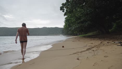 Ein-Einsamer-Mann-Geht-Am-Sandstrand-Mit-Ruhigen-Wellen-Am-Strand-Von-Dam-Trau-Auf-Der-Insel-Con-Dao-In-Vietnam-Entlang