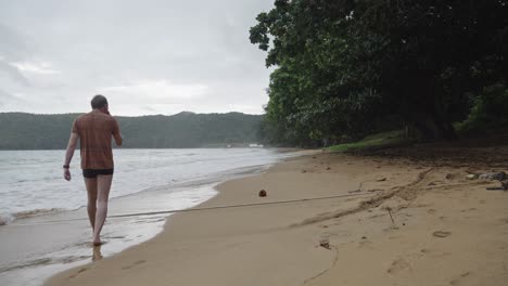 un hombre solitario camina por la playa de arena con olas tranquilas en la playa de dam trau, isla de con dao, vietnam