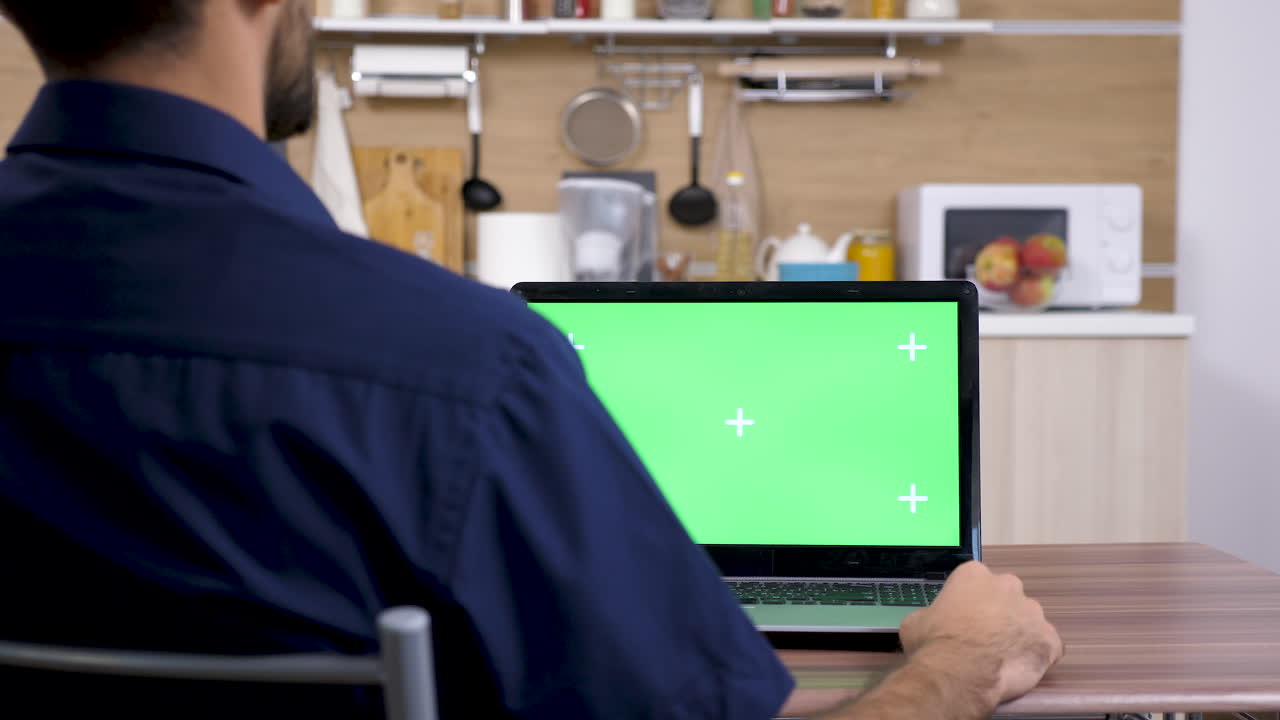 Man working on laptop with green screen in kitchen