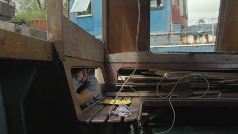 young man wearing mask painting underside of deck interior wooden boat cabin