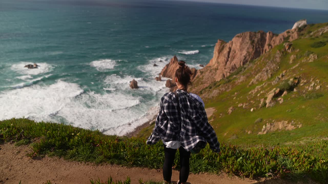 mujer caminando por un acantilado con vistas al océano