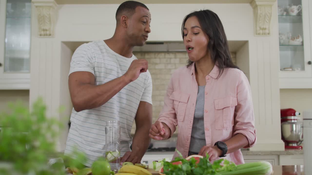 Happy biracial man feeding woman with vegetables in kitchen
