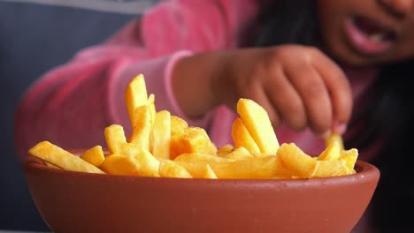 un niño alcanzando papas fritas en un tazón marrón