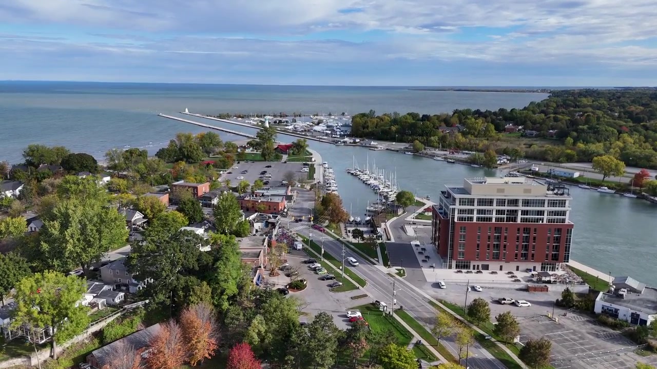 Vista aerea con drone di una cittadina costiera con porto turistico in Canada, con porto, edifici sul lungomare, barche, strade e la tranquilla riva di un lago sotto un cielo diurno nuvoloso