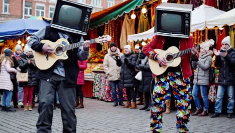 artistas callejeros con cabezas de televisión tocando guitarras en un mercado de navidad