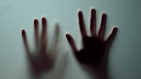 Macro-two-female-hands-pressing-against-glass-wall-indoors.Blurred-hands-shadow.