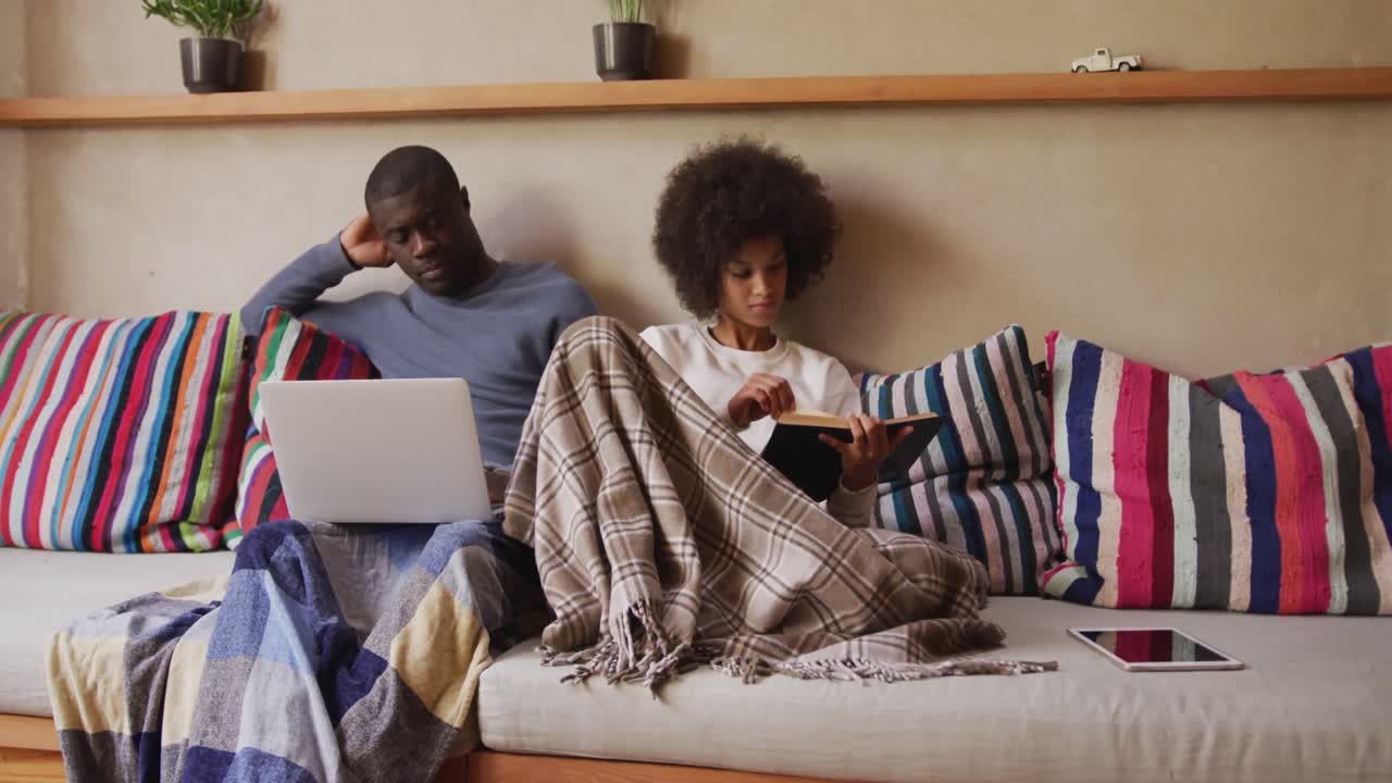 Couple sitting on the couch reading and using computer