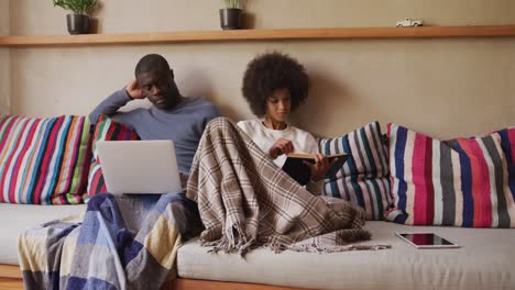 Couple-sitting-on-the-couch-reading-and-using-computer