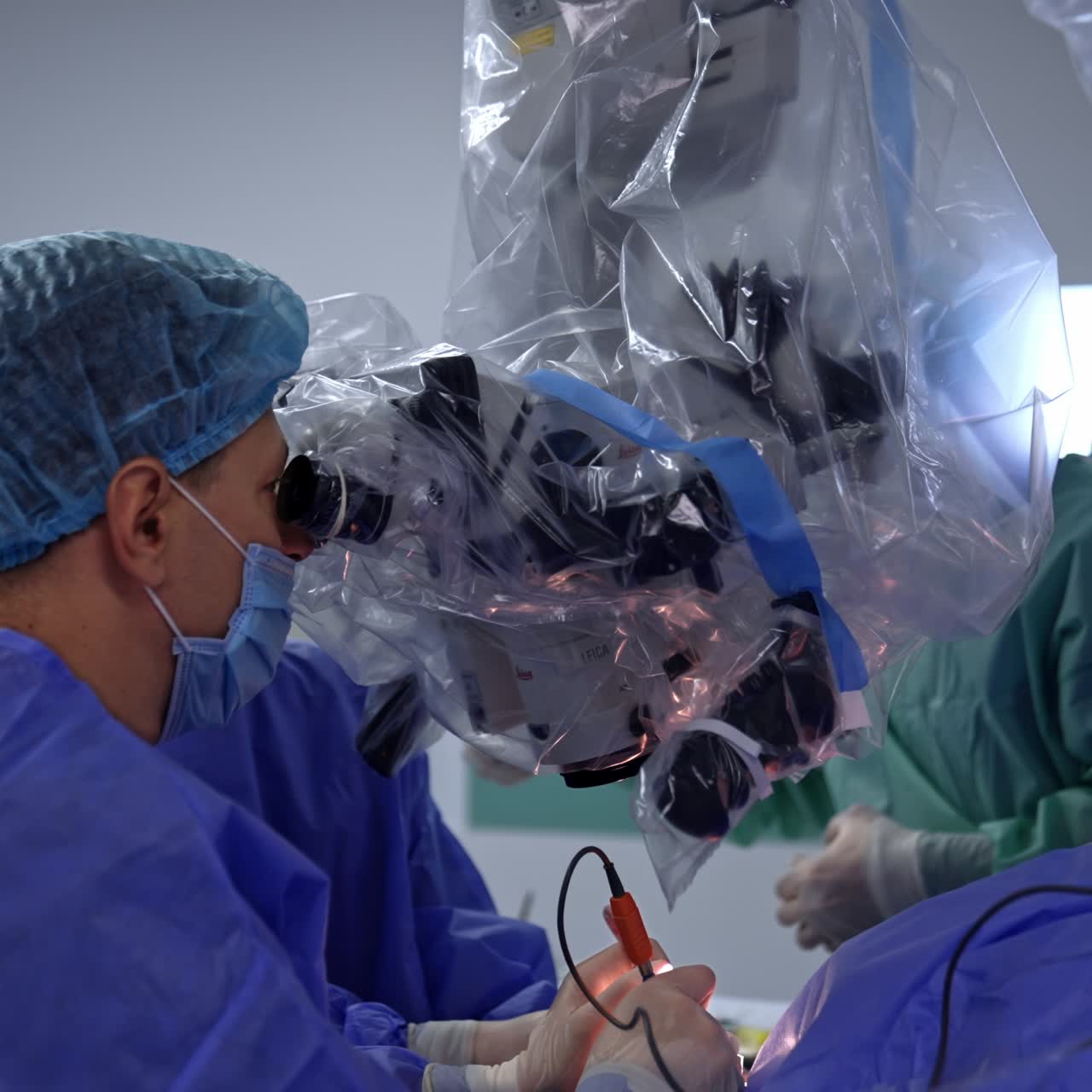 Experienced specialist conducting surgery in neurology. Surgeon looking at the binocular of microscope and applying electric tools