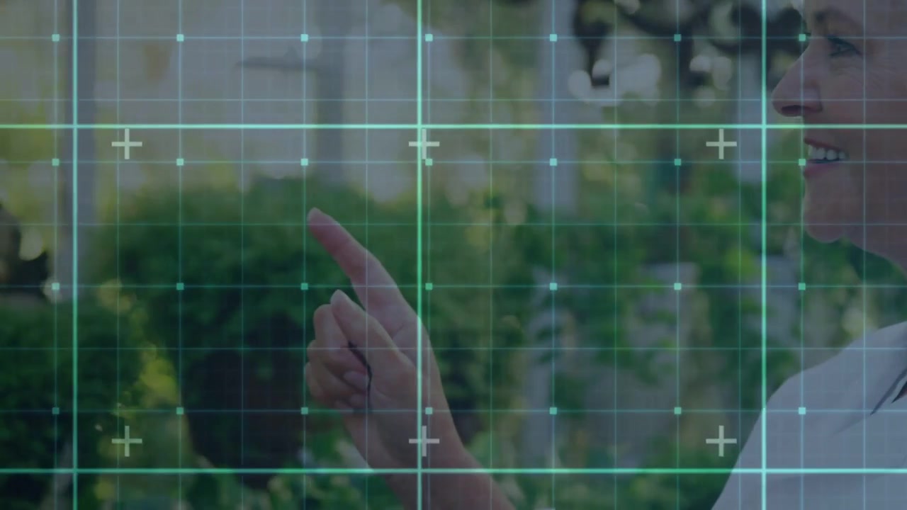 Senior woman raising finger and tapping holographic grid by glass, tablet guiding AR garden design