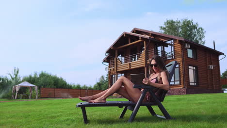 a beautiful sexy woman lying on a sun lounger in the backyard of her mansion is doing online shopping with a tablet computer