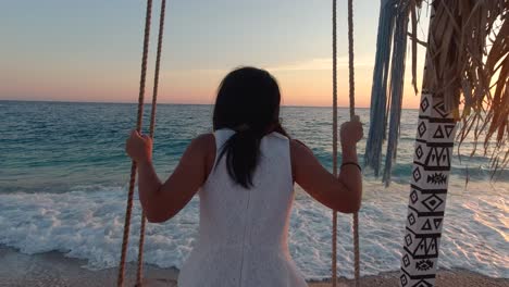 slow motion girl swinging on bench next to beautiful ocean at sunset