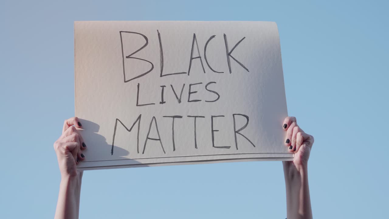 Hands Holding 'Black Lives Matter' Sign Against Blue Sky