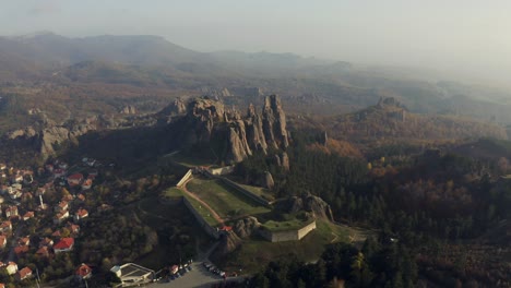 Panoramic-aerial-view-of-the-historical-Belogradchik-village-in-Bulgaria,-featuring-rock-formation,-medieval-fortress-and-town,-surrounded-by-greenery
