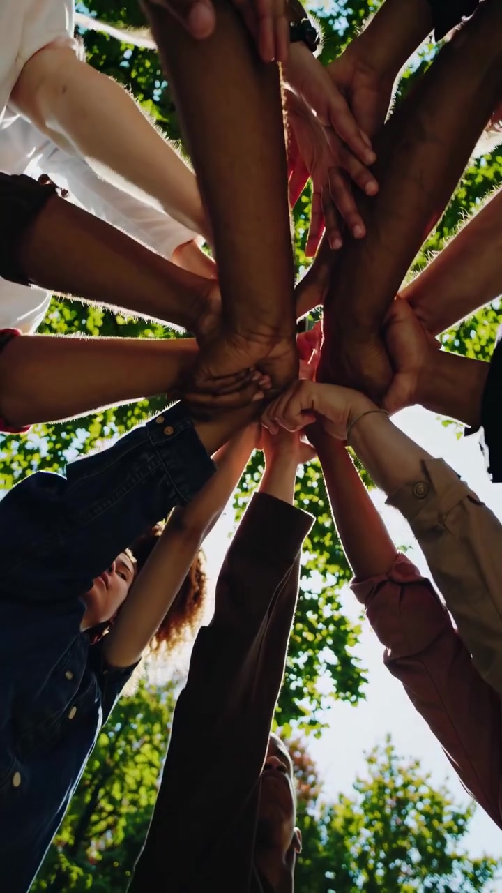 Diverse Group of People Joining Hands in a Circle Under Green Trees