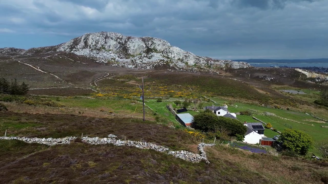 Exuberante paisaje verde de páramos galeses en la base de la cima de la montaña Holyhead, con cabañas y tierras de cultivo.