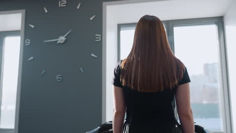 girl walking on treadmill in modern gym with sunlight reflecting off her hair and arm while exercise bikes and elliptical trainer stand under bright windows