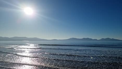 Slow-motion-tide-waves-splashing-under-dreamlike-hazy-sunrise-Snowdonia-mountain-range-skyline