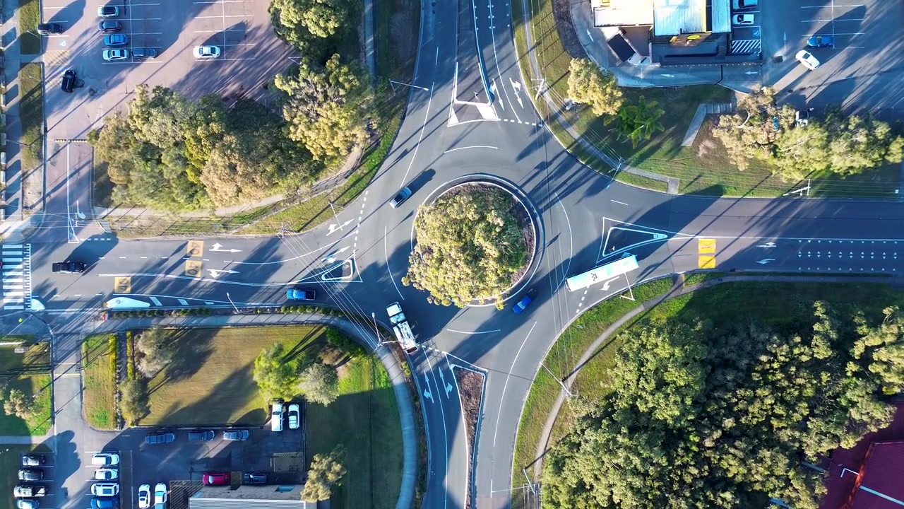 Drone aerial landscape of car vehicles and a truck driving through a roundabout road junction surrounded by a public carpark and commercial buildings in Bateau Bay Central Coast Australia transport