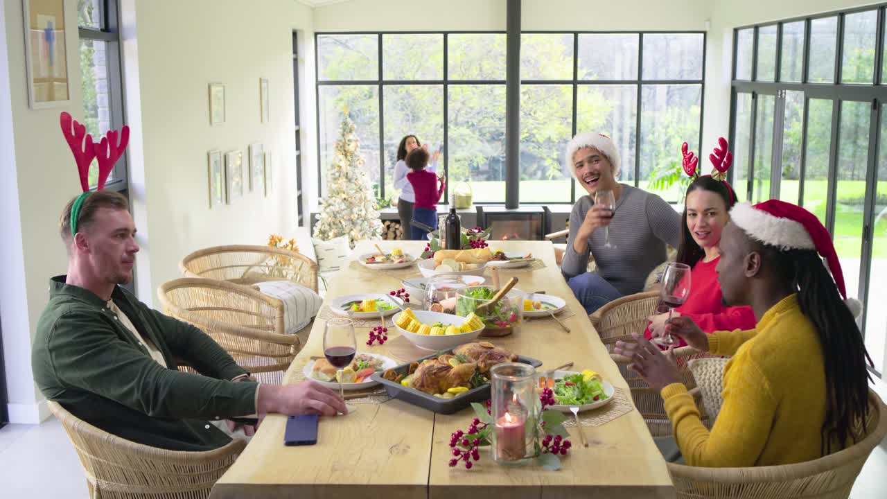 Diverse friends at dining table are toasting wine glasses after window gesture drawing surprise