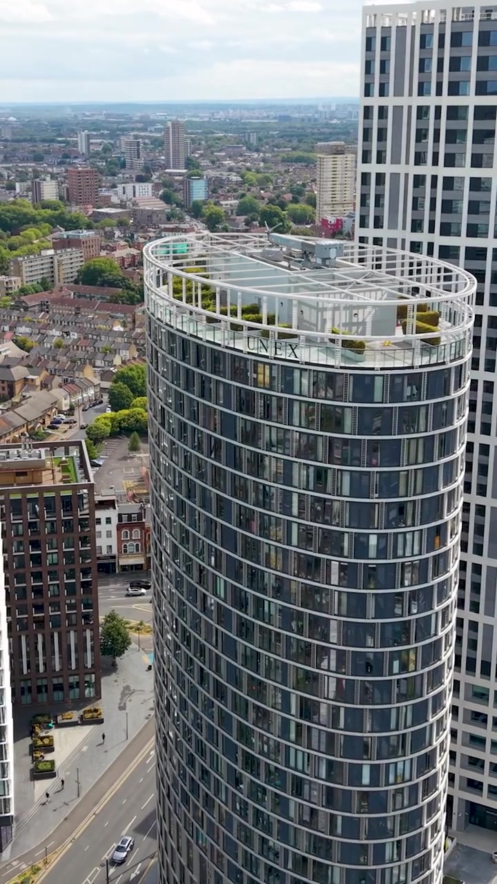 Blocos de torres Stratosphere e Stratford Eye em órbita de drone à direita em Stratford, Londres, revelando arquitetura moderna de arranha-céus, linhas férreas e casas do East End sob nuvens diurnas claras. Vertical