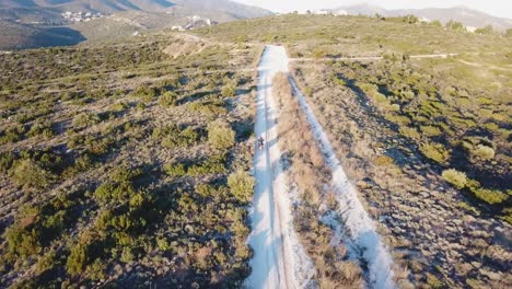 aerial shot of following a motorcyclist while he drives on gravel road during golden hour on a mountain next to athens, greece