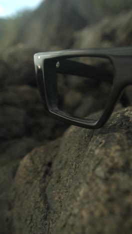 glasses resting on a rock in a natural outdoor environment, soft focus on the frame
