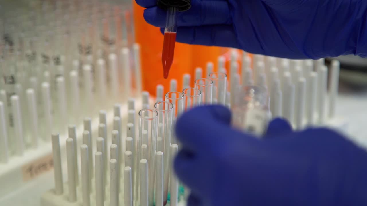 A lab tech uses a pipette to fill vials with a red liquid for a science experiment