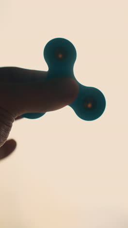 cu: silhouette of young man hand holding turning spinner against bright sun backlight near window in room extreme close view