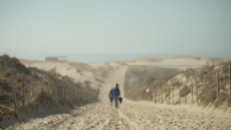 Blurry View Of Two People Walking Along A Dusty Unpaved Road Through The Wilderness . - Defocused, Slow Motion