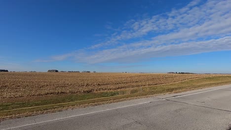 pov through drivers side window while driving down a rural county road in late afternoon past harvested fields and farms on a sunny day